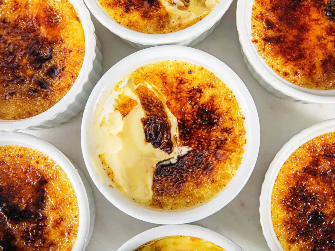 Mehrere cremige Cr&egrave;me br&ucirc;l&eacute;e Desserts in wei&szlig;en F&ouml;rmchen, mit knuspriger Karamellkruste und Vanillecreme.