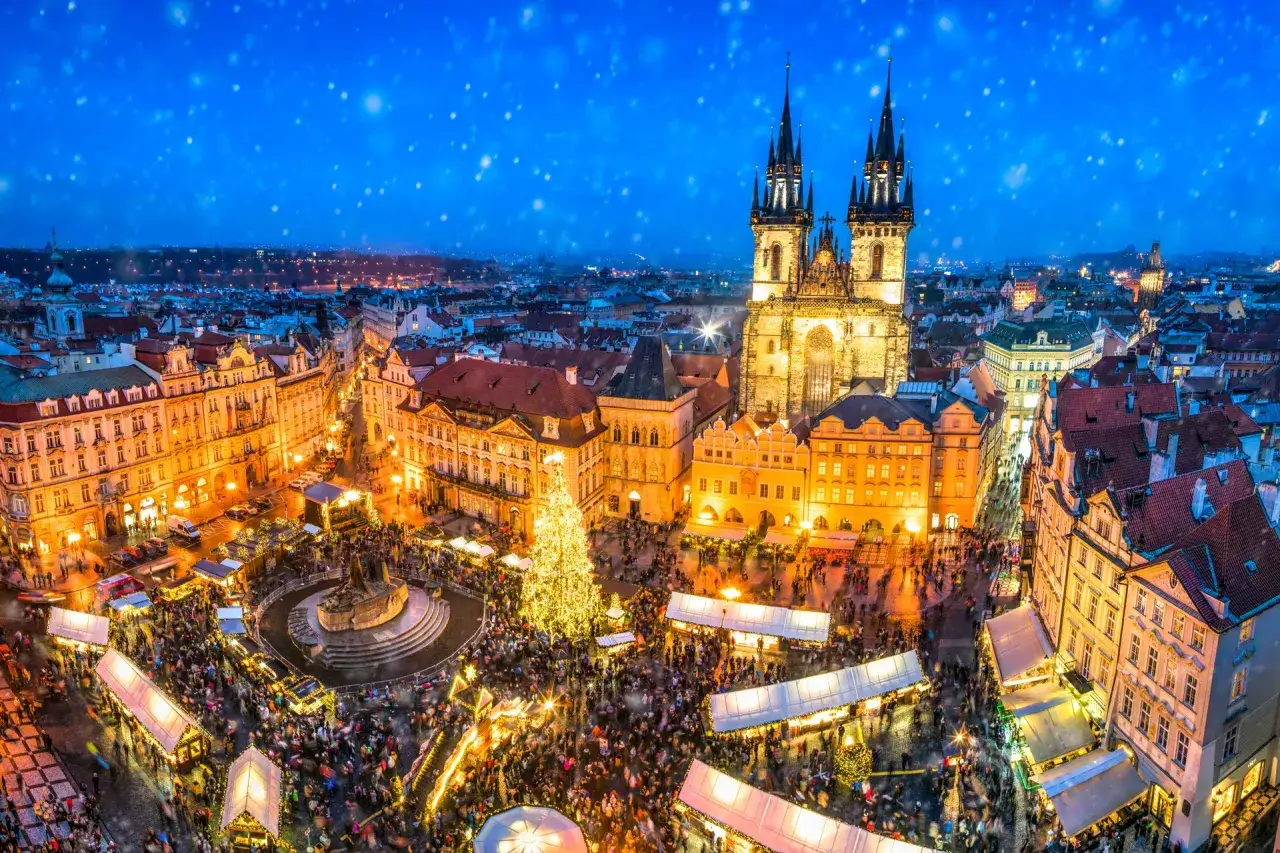 Tłumy ludzi na jarmarku bożonarodzeniowym w Czechach, w tle zabytkowa architektura i oświetlona choinka.