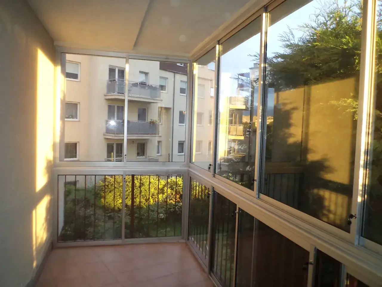 Zabudowany balkon w bloku z wielkiej płyty. Widok na sąsiedni budynek i zieleń. Poznaj prawdziwe koszty dobudowy zewnętrznych balkonów.