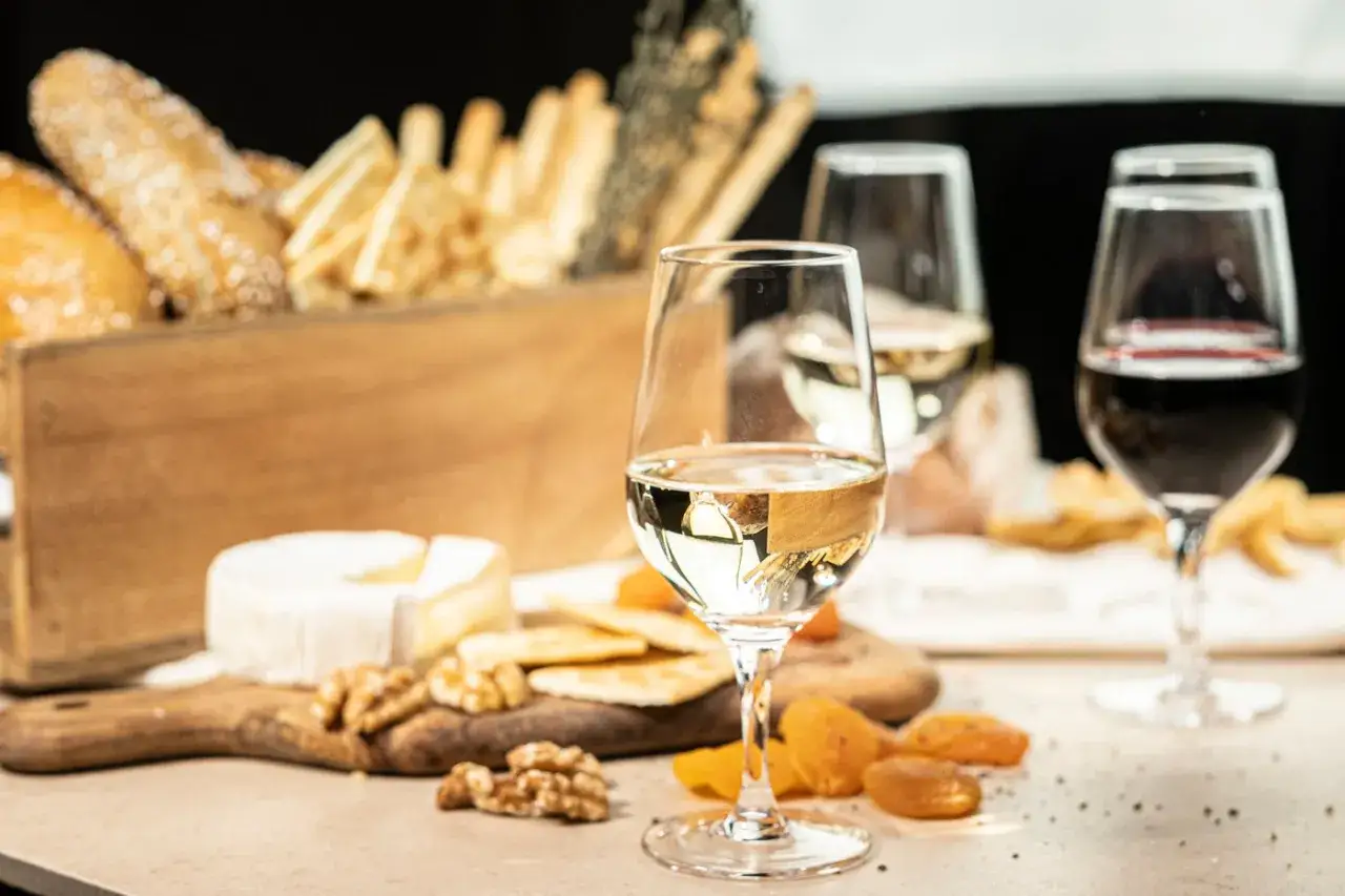 Ein Glas Wei&szlig;wein, daneben K&auml;se, N&uuml;sse und Trockenfr&uuml;chte. Im Hintergrund ein Glas Rotwein und Brot. Was ist Portwein? Ein s&uuml;&szlig;er, aufgespriteter Wein.