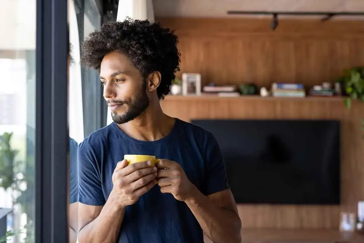 Uomo con tazza gialla, forse una bevanda calda per stitichezza, guarda fuori dalla finestra.