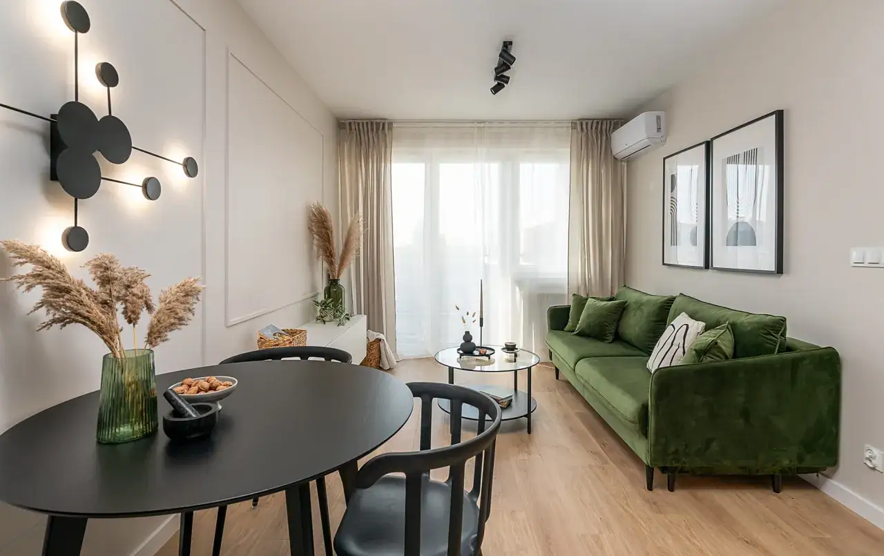 Jak urządzić małe mieszkanie 40 m: zielona sofa, czarny stół, nowoczesna lampa i dekoracje tworzą przytulną przestrzeń.