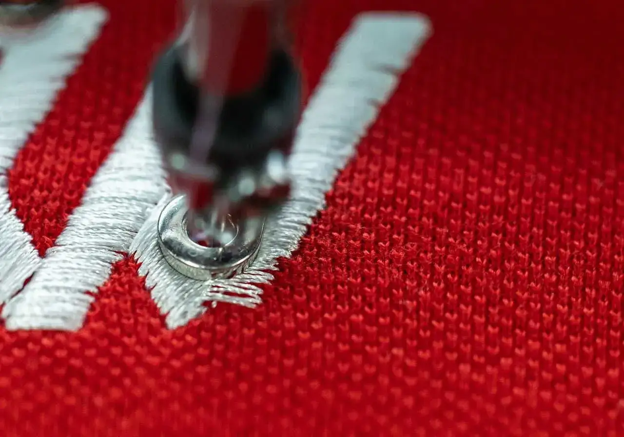 Gros plan sur une machine de **direct to garment printing** cr&eacute;ant un motif blanc sur un tissu rouge.