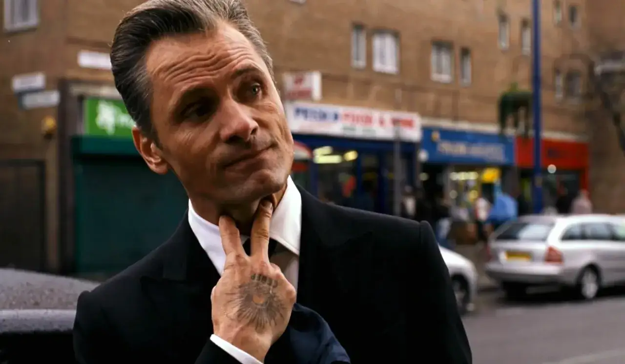 Viggo Mortensen w garniturze, z dłońmi na szyi, w kadrze z ulicy. Jego filmy często pokazują go w takich mrocznych rolach.