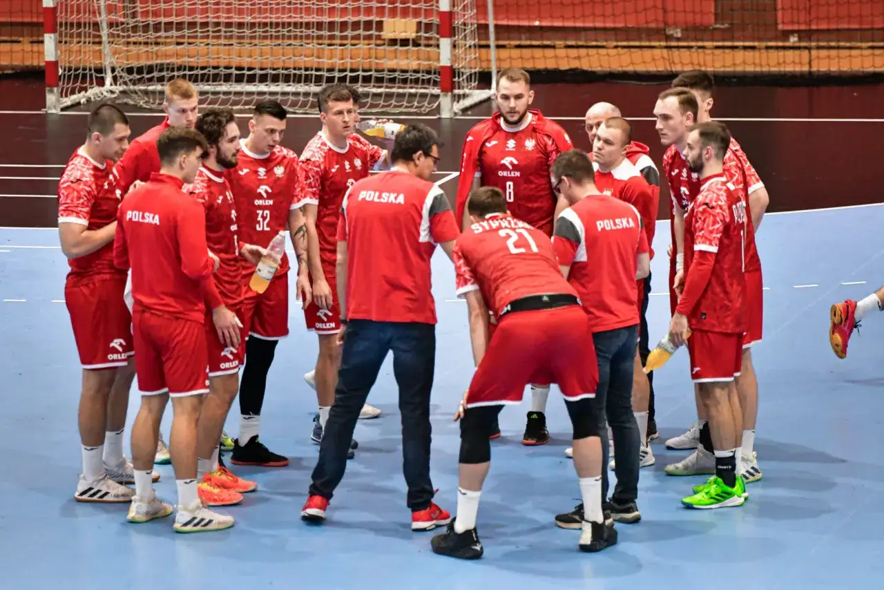 Drużyna piłkarzy ręcznych Polski w czerwonych strojach omawia taktykę. To ważny moment przed meczem w ramach Mistrzostw Europy.