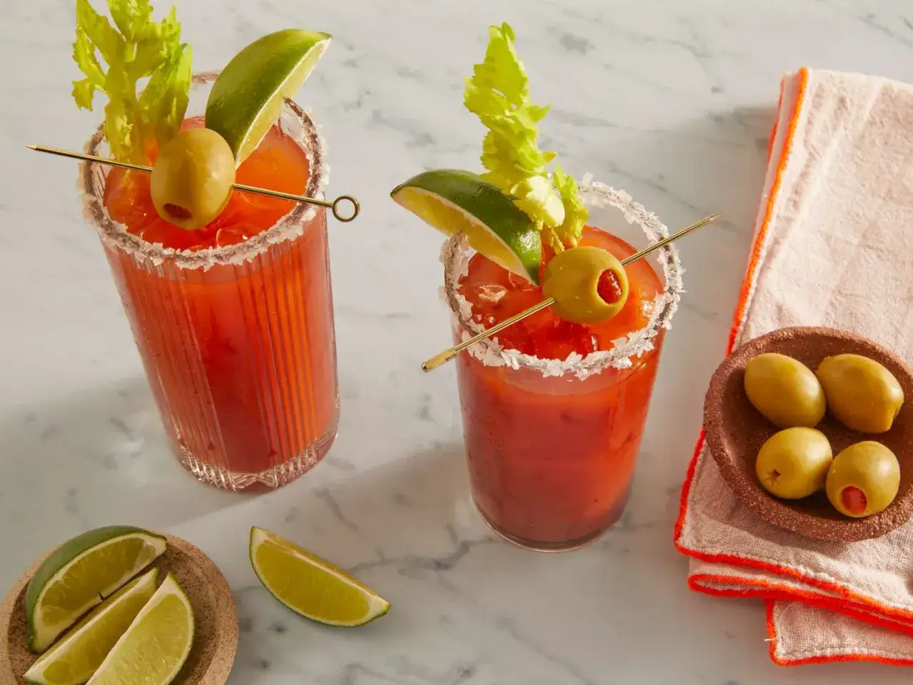 Två Bloody Mary-drinkar med saltkant, garnerade med oliv, lime och selleri. En perfekt start på helgen!