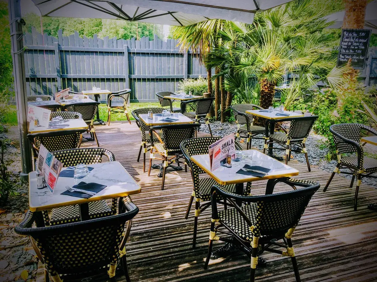 Terrasse d'un restaurant, tables dressées sous un parasol, ambiance estivale. Un lieu authentik à St Grégoire pour un repas en plein air.