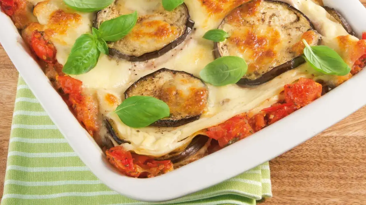 Herzhafte Auberginen Lasagne mit geschmolzenem Käse und frischem Basilikum, serviert in einer weißen Auflaufform.