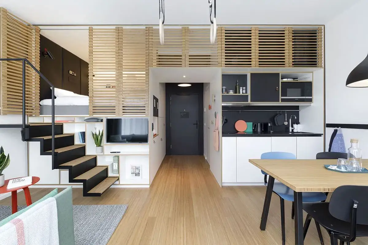 Idée aménagement petit appartement : lit mezzanine, escalier avec rangements, cuisine compacte et coin repas. Optimisation de l'espace.