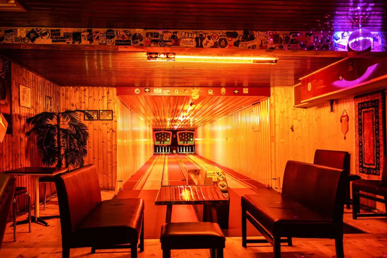 Gem&uuml;tliche Kegelbahn in Berlin mit Holzvert&auml;felung, roten Ledersitzen und einer Discokugel.