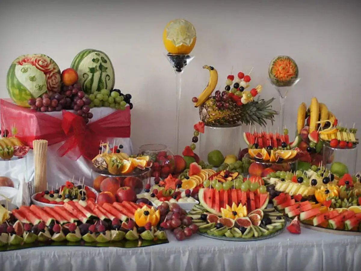 Elegancka patera z owocami na wesele, pełna kolorowych arbuzów, winogron i melonów, ozdobiona rzeźbami.