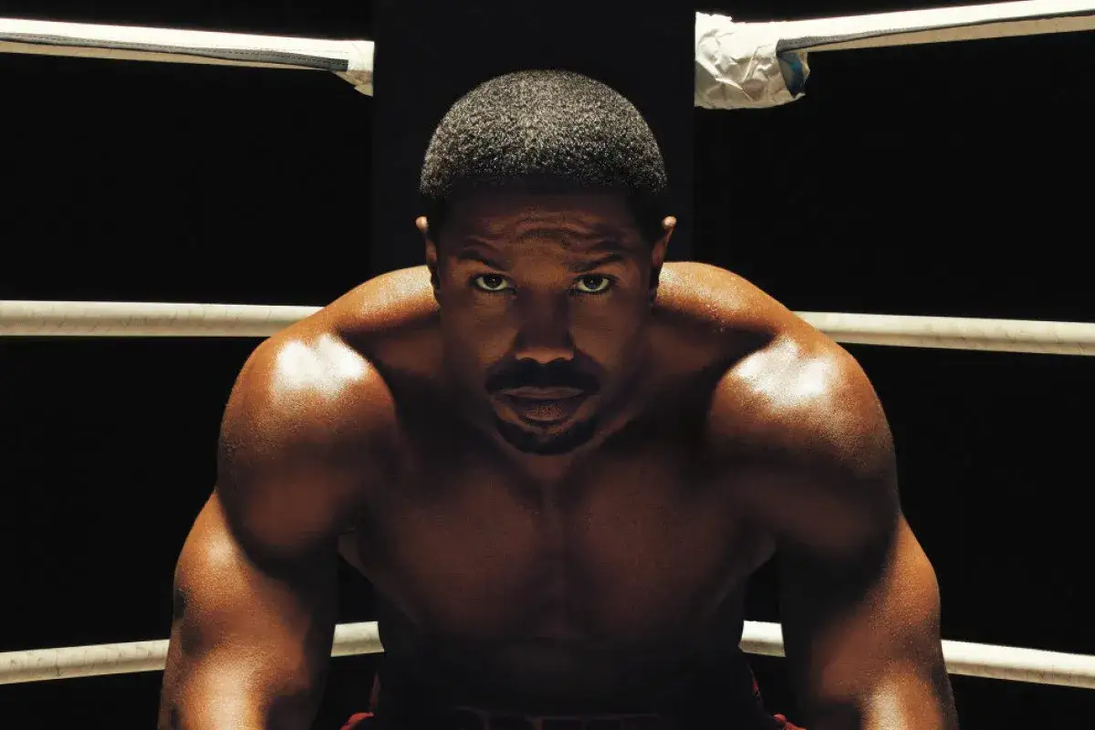 Zdeterminowany bokser, Adonis Creed, w ringu, gotowy do walki. Jego spojrzenie mówi wszystko o jego determinacji i sile.