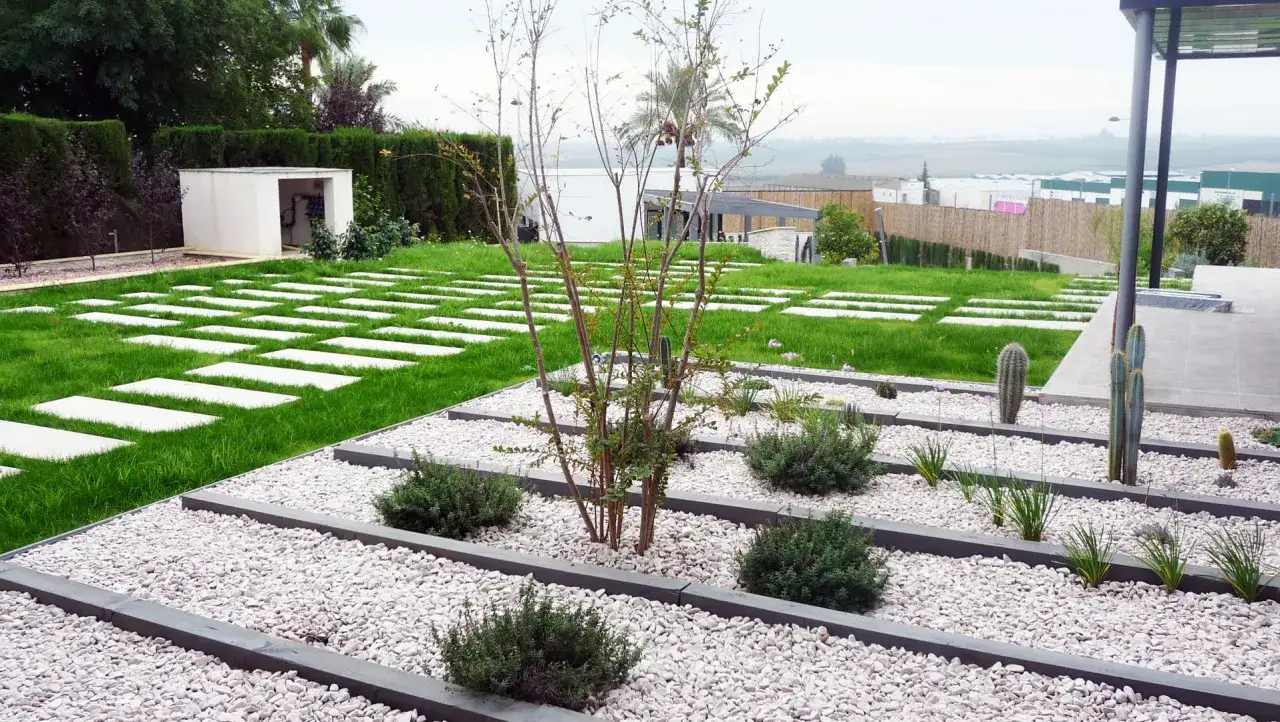 Vialetti giardino moderni con lastre quadrate su prato e aiuole di ghiaia bianca con piante succulente e arbusti.