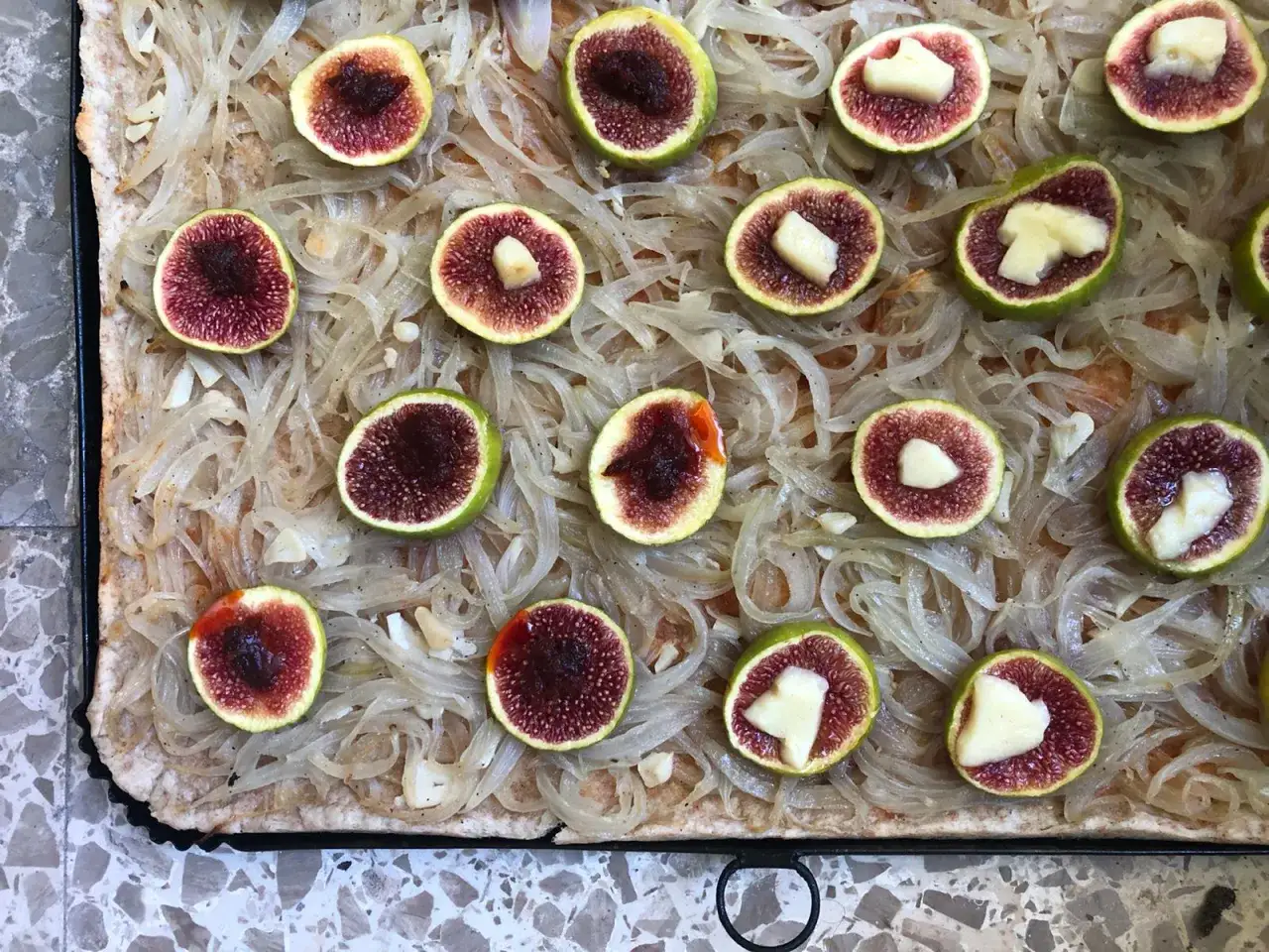 Coca mallorquina con higos frescos y queso. Una base crujiente cubierta de cebolla caramelizada y coronada con mitades de higo, algunas con trozos de queso.