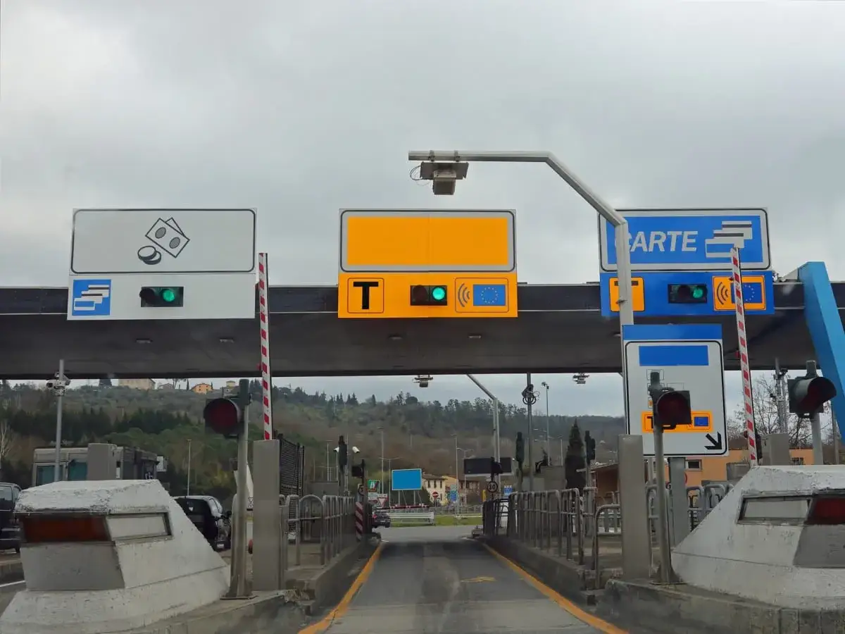 Casello autostradale con segnali per Telepass UnipolMove e pagamenti elettronici. Semafori verdi indicano corsie aperte.