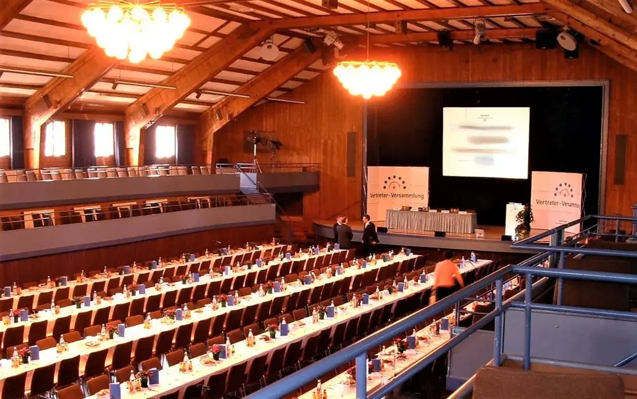 Gro&szlig;er Saal der Stadthalle Herrenberg mit langen Tischen, St&uuml;hlen und B&uuml;hne.