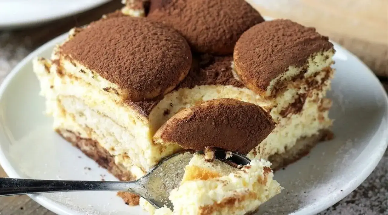 Pyszne ciasto san francisco, warstwowe tiramisu posypane kakao, z widelcem nabierającym kawałek.