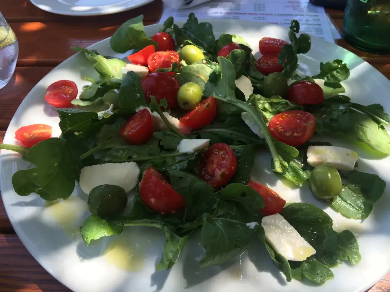 Frischer Rucola Salat mit Kirschtomaten, Mozzarella und grünen Oliven, beträufelt mit Olivenöl.