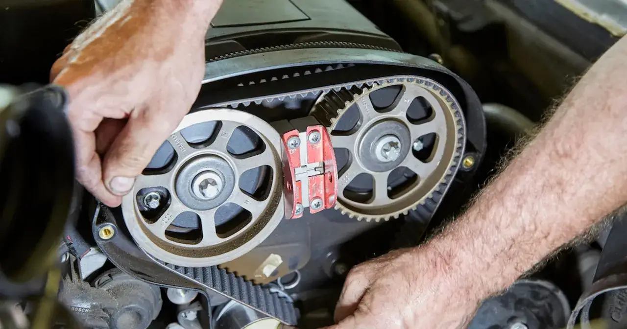 Mechanik precyzyjnie montuje nowy pasek podczas wymiany rozrządu w silniku samochodowym.