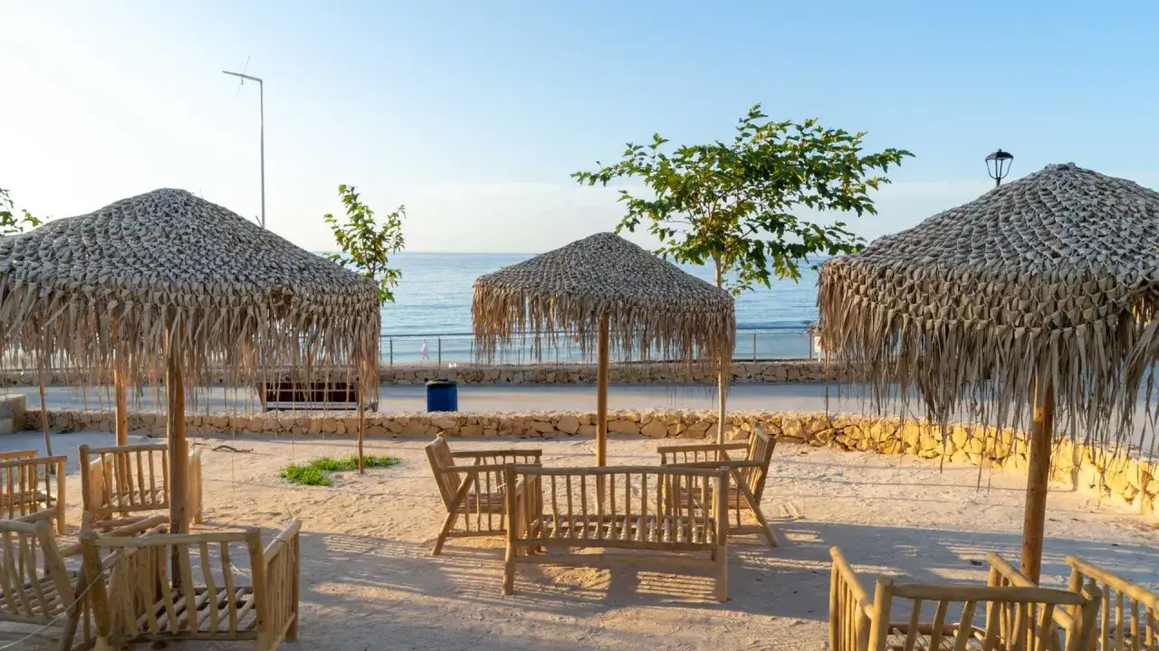 Un rincón de cala Lanuza con sombrillas de paja y mobiliario de madera, listo para disfrutar del mar.