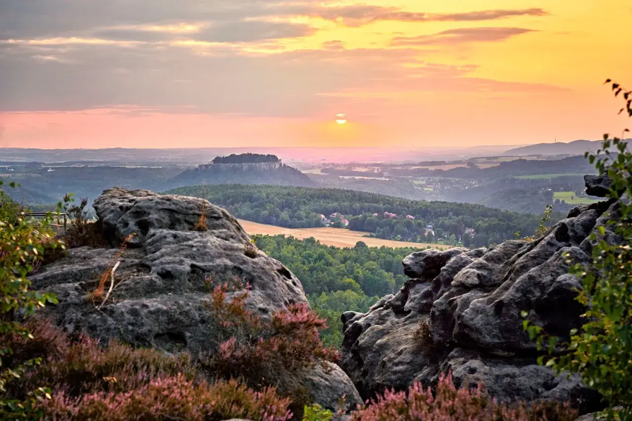 Sonnenuntergang über dem Elbsandsteingebirge. Ein perfekter Ort für eine Schmilka Wanderung, mit Felsen und Heidekraut im Vordergrund.