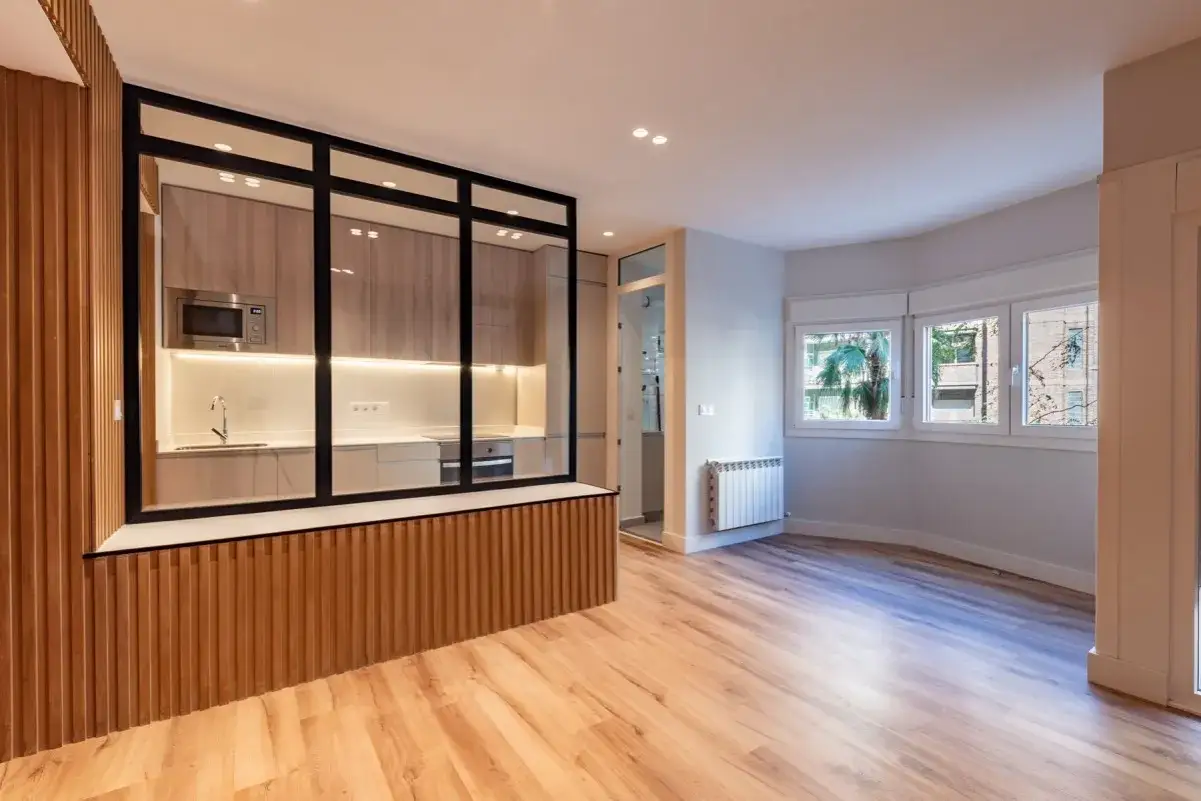 Entrada salón recibidor integrado con cocina moderna y luminosa, separada por cristal y madera. Amplio espacio diáfano con suelo de parquet.
