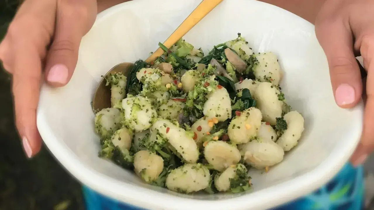 Pyszne gnocchi z pesto, brokułami i płatkami chili w białej misce, trzymanej przez dłonie.