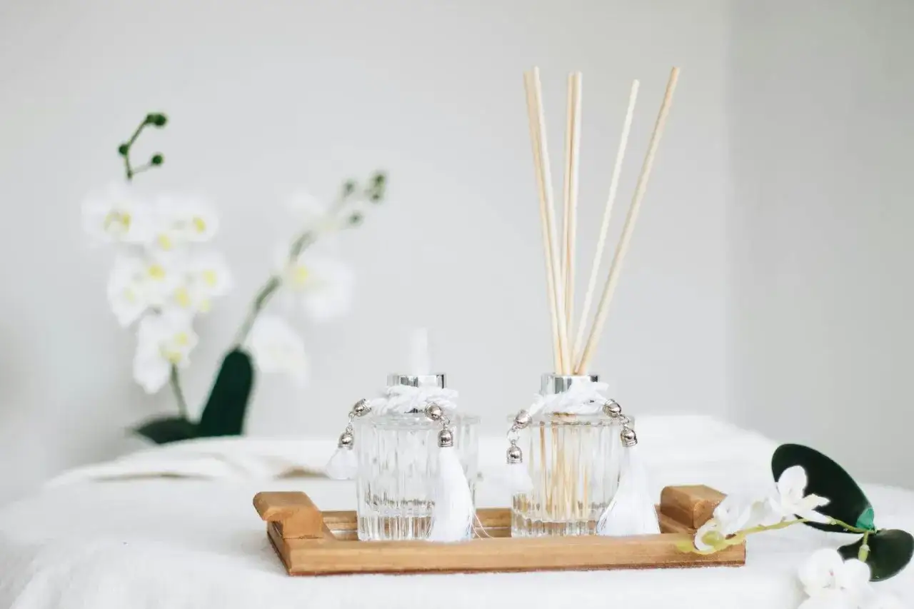 Deux diffuseurs de parfum élégants sur un plateau en bois, créant un **arôme intérieur** apaisant, avec des orchidées blanches en arrière-plan.
