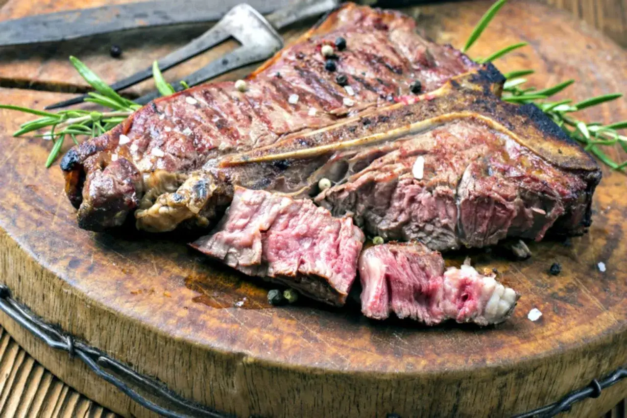 Una succulenta bistecca fiorentina, tagliata e pronta per essere gustata, adagiata su un tagliere di legno con rosmarino e grani di pepe.