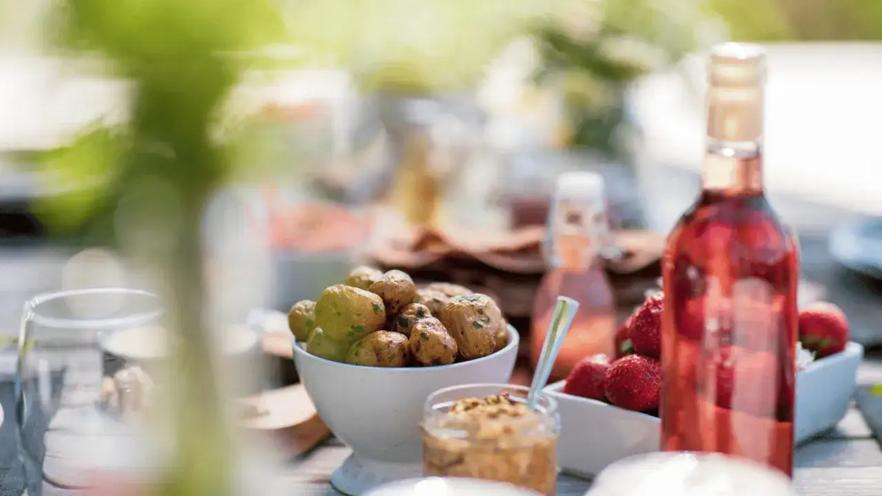En flaska rosévin till midsommar, med färskpotatis och jordgubbar på ett dukat bord utomhus.