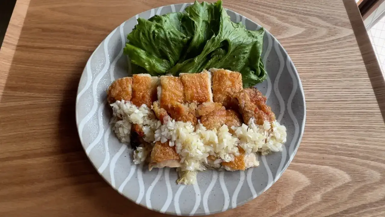 Chrupiące karaage z kurczaka, posypane posiekanym czosnkiem, podane z sałatą na talerzu.