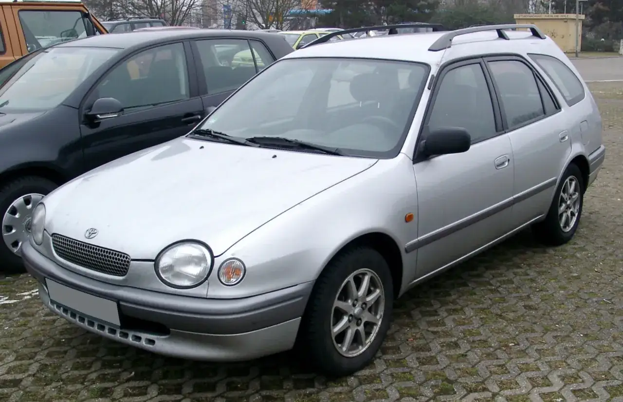 Srebrne kombi Toyota Corolla E11 z relingami dachowymi zaparkowane na kostce brukowej.