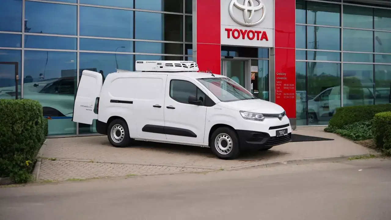 Biały furgon z chłodnią na dachu zaparkowany przed salonem Toyoty.