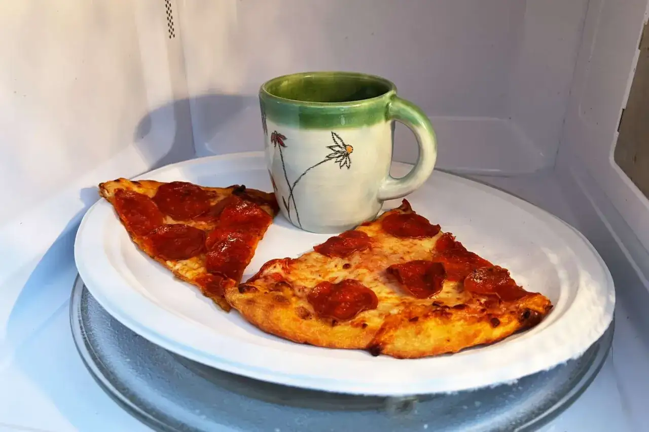 Dwie kromki pizzy Giuseppe i kubek z kwiatami czekają na podgrzanie w mikrofali.