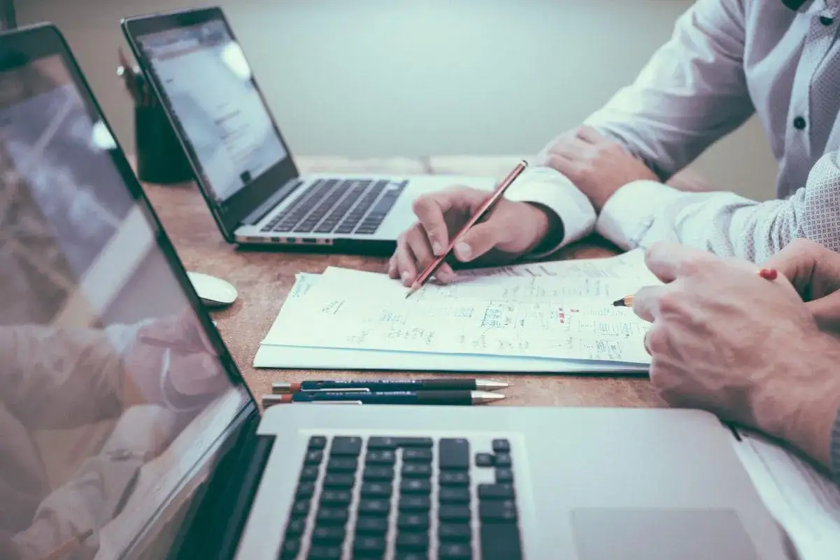 Dwie osoby pracują nad projektem, analizując dokumenty i notatki przy laptopach. To praca zespołowa, gdzie każdy wnosi swój wkład, by osiągnąć wspólny cel.