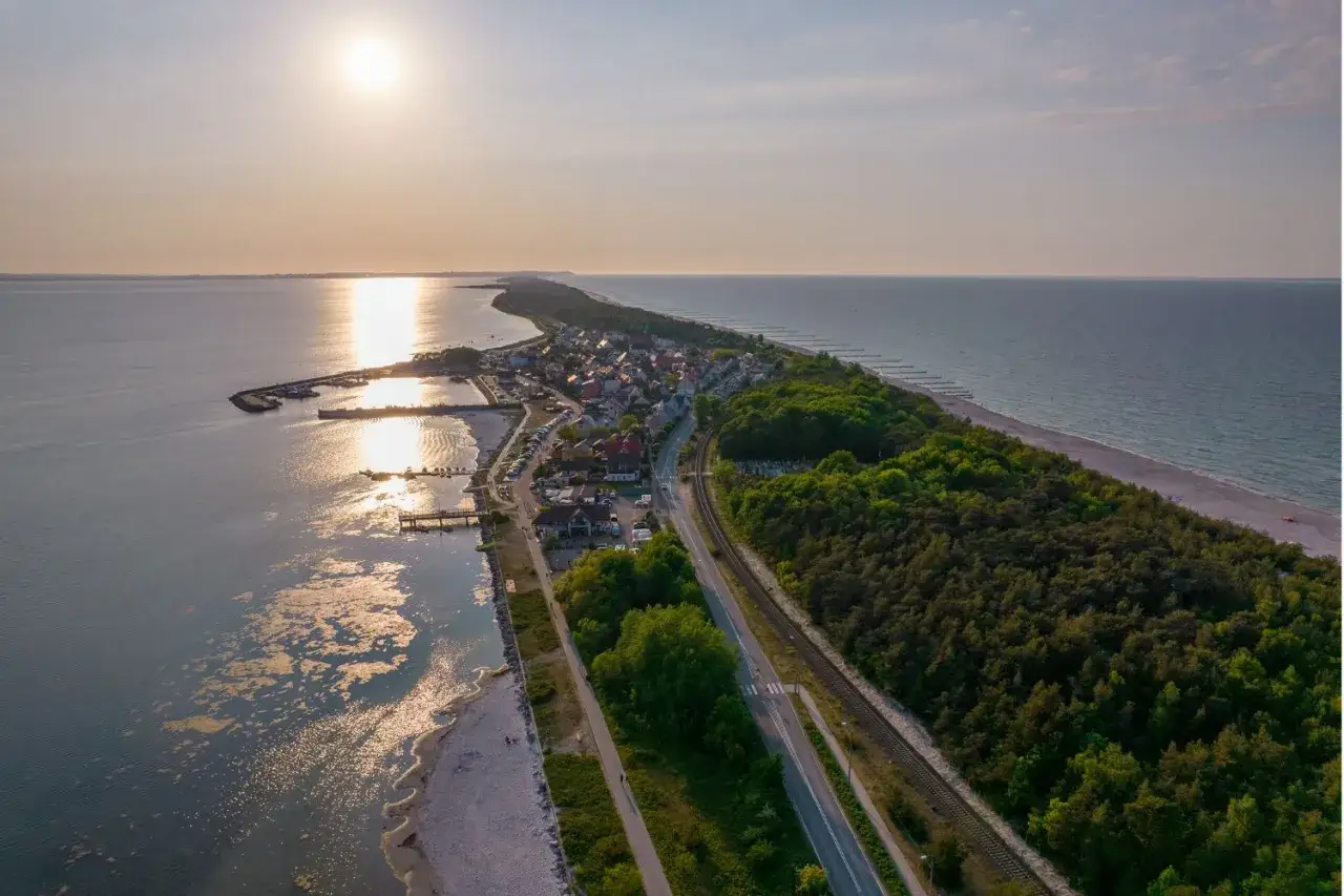 Malownicze widoki na Mierzeję Wiślaną, idealne na jednodniowe wycieczki z Gdańska. Słońce odbija się w wodzie, a lasy otaczają urokliwą miejscowość.
