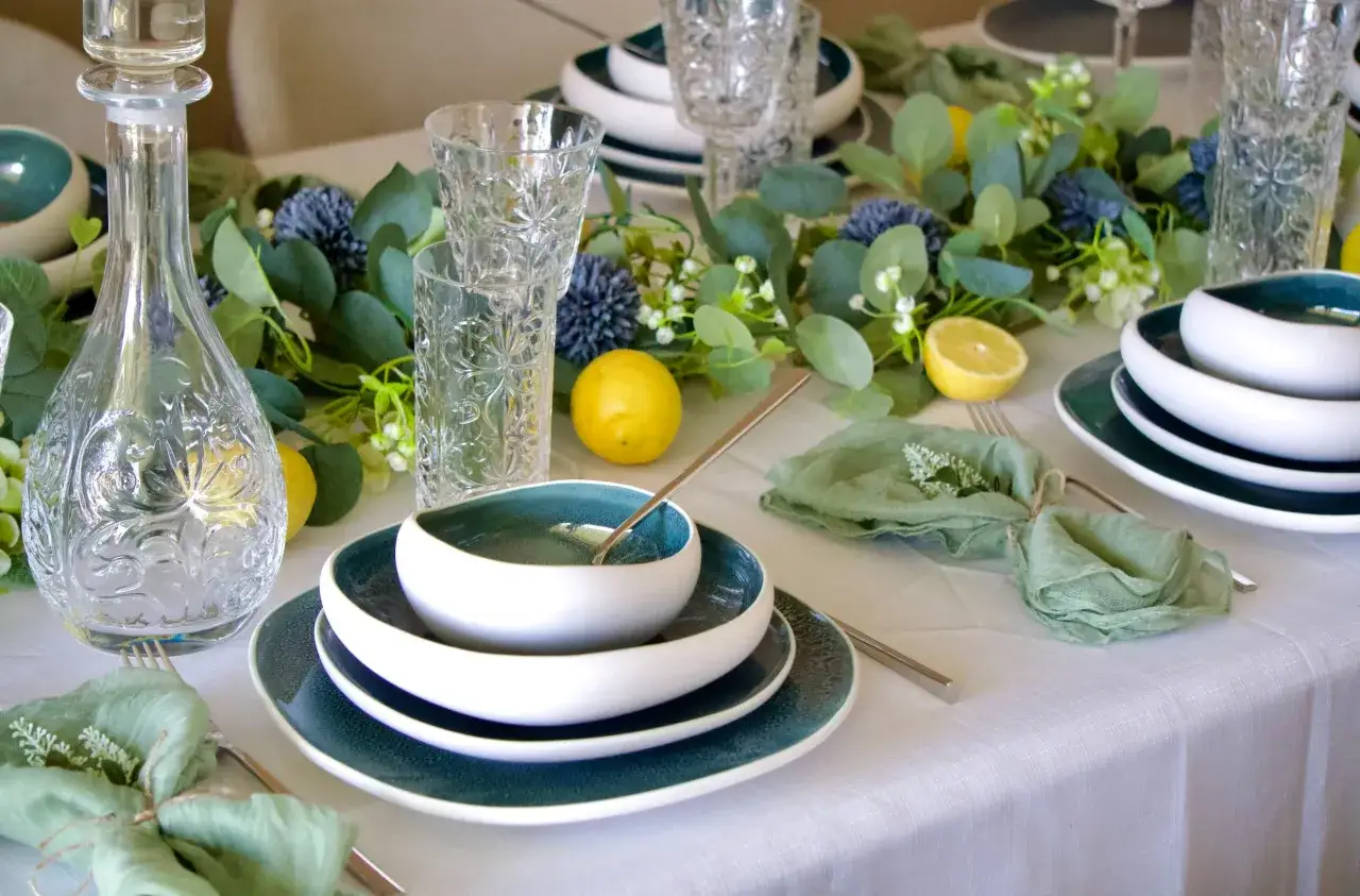 Une table dressée avec élégance, des assiettes bleues et blanches, des verres ciselés, des citrons et une carafe en cristal, invitant aux arts de la table.