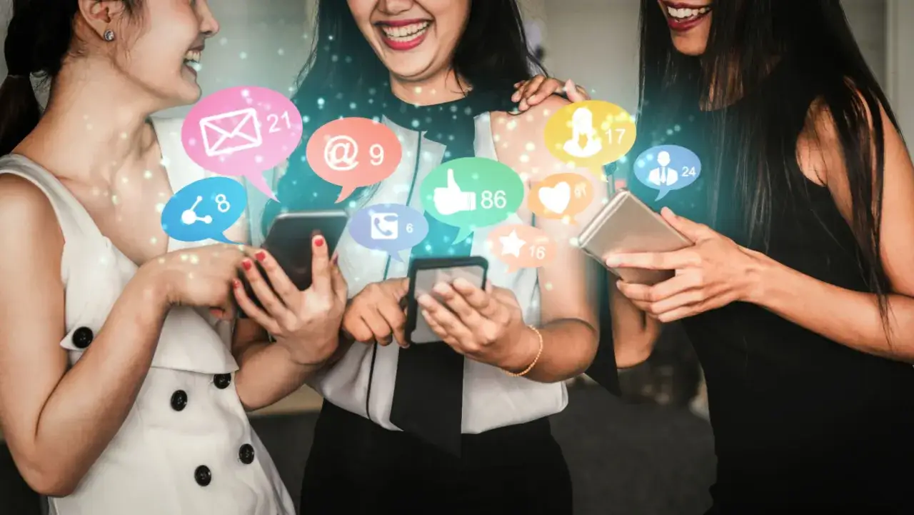 Trzy kobiety śmieją się, przeglądając swoje telefony, otoczone ikonami powiadomień z social mediów.