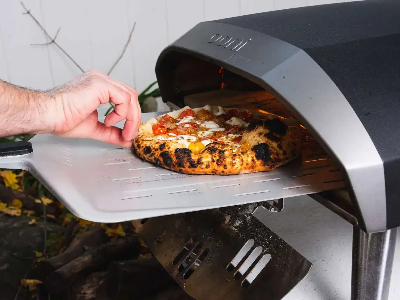 Ręka wyjmuje z pieca pizzę. Idealna do pieczenia w wysokiej temperaturze, by uzyskać chrupiące ciasto.