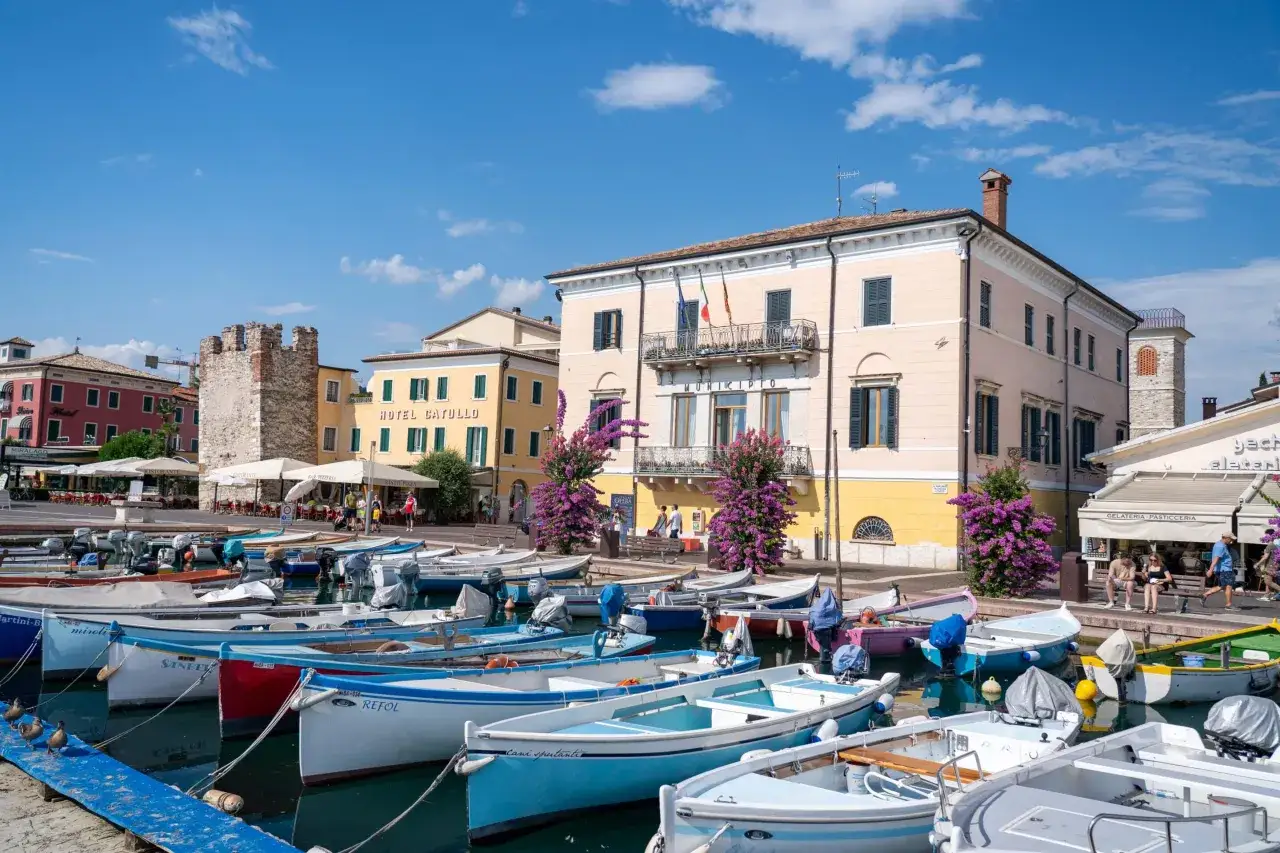 Bateaux amarrés dans un port pittoresque, avec des bâtiments colorés et une tour médiévale. Idéal pour savoir que faire au lac de Garde.