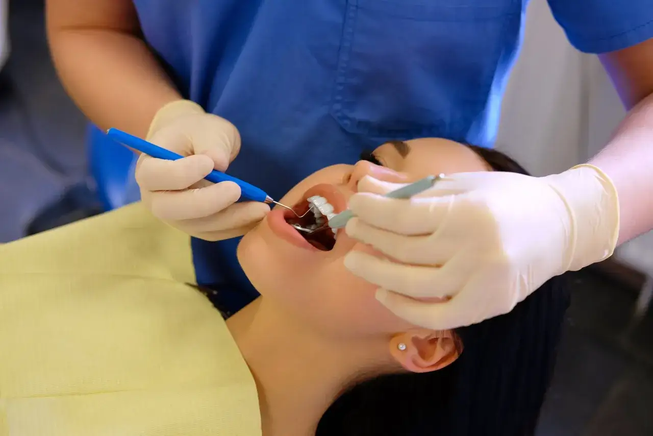 Dentysta wykonuje zabieg szynowania zębów na NFZ. Pacjentka ma otwarte usta, a lekarz używa narzędzi.