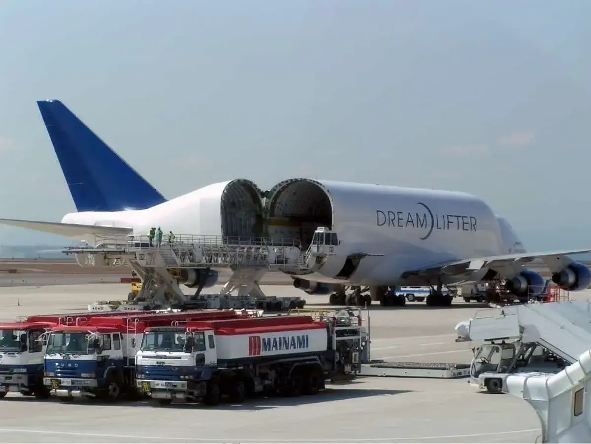 Der Dreamlifter mit ge&ouml;ffnetem Rumpf steht bereit. Mehrere Tankwagen warten auf dem Rollfeld.