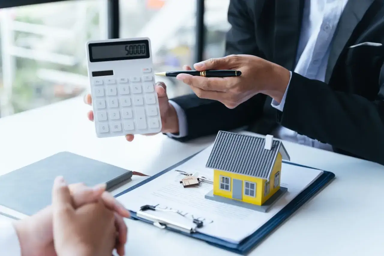 Conseiller montrant une calculatrice et une maquette de maison, symbolisant l'aide au premier achat immobilier.