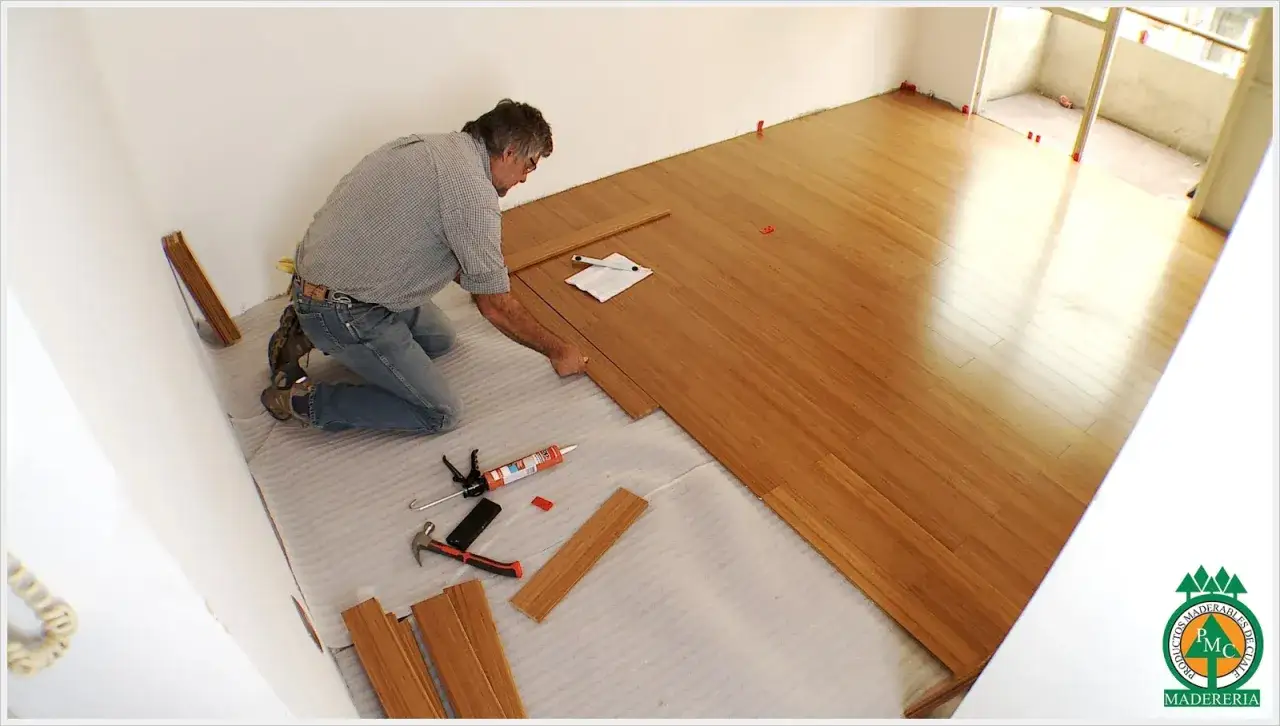 Hombre instalando suelo de madera sobre cemento. Herramientas y adhesivo listos para continuar.