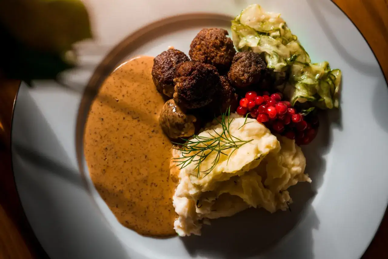 En tallrik med klassiska svenska r&auml;tter: k&ouml;ttbullar, potatismos, gr&auml;dds&aring;s, lingon och pressgurka.