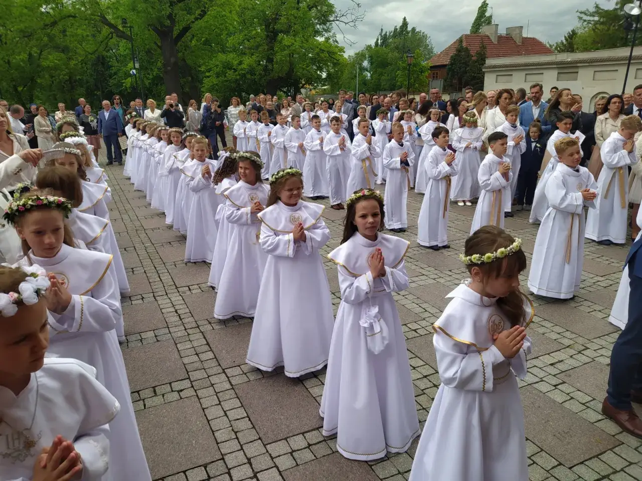 Dzieci w białych albach, gotowe do I Komunii Świętej, stoją w rzędzie. Czy komunia jest obowiązkowa? To ważne pytanie dla wielu rodzin.