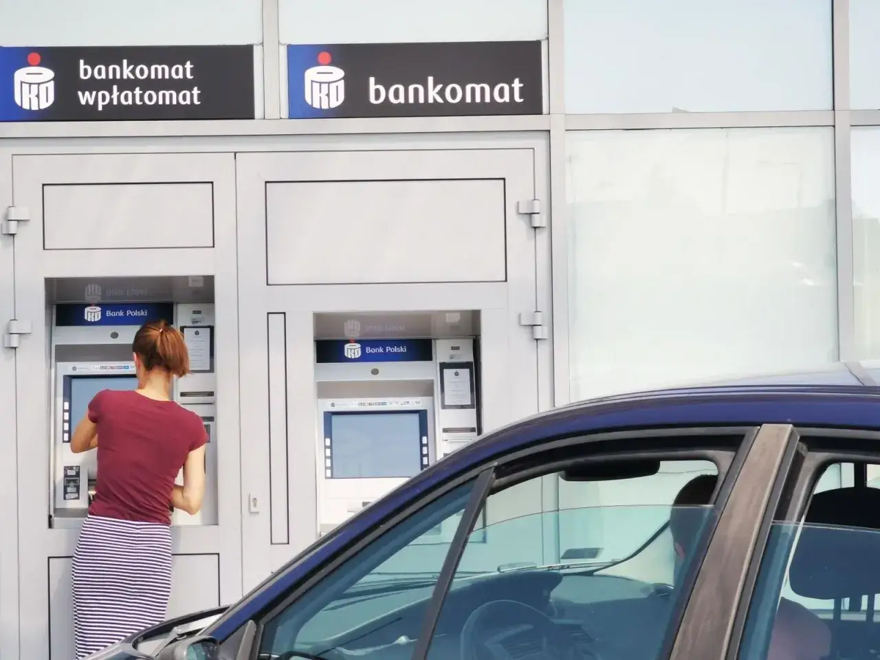 Kobieta dokonuje pko wypłata gotówki w oddziale banku przy bankomacie.