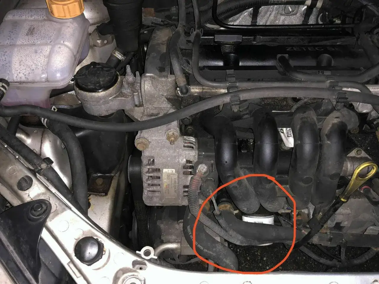 Motorraum mit rotem Kreis um eine undichte Wasserpumpe. K&uuml;hlmittelbeh&auml;lter und Zylinderkopf sichtbar.