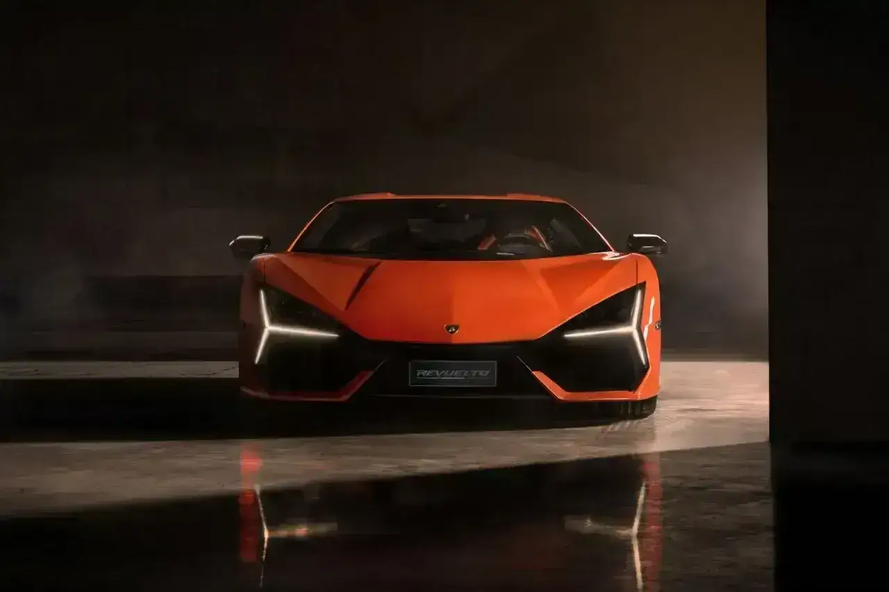 Pomarańczowy Lamborghini Revuelto z ostrymi światłami LED, odbijający się w mokrej podłodze.