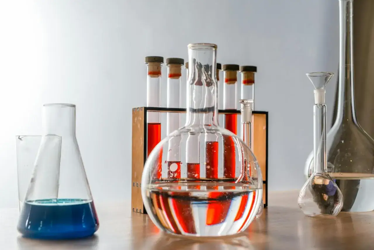 Laboratorium bada zawartość chloru w wodzie z kranu. Kolby i prob&oacute;wki z płynami w r&oacute;żnych kolorach stoją na drewnianym blacie.